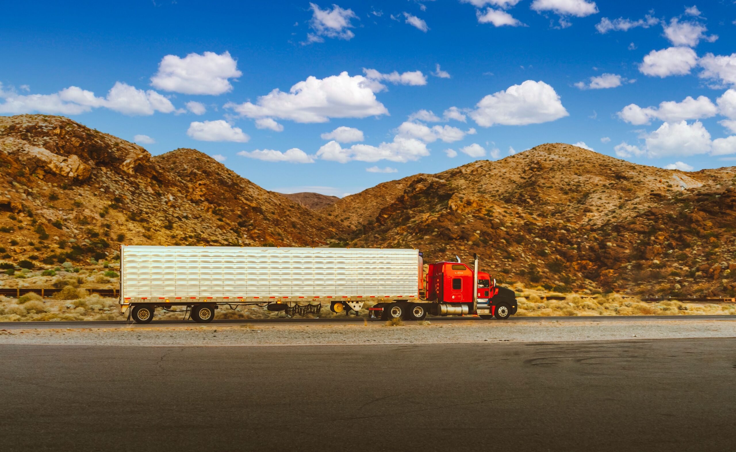 Red semi-truck with unbranded trailer on a highway (desert backdrop &mdash; generic commercial-trucking visual, not Virginia s