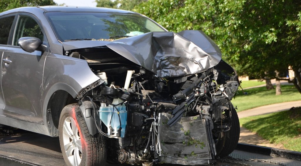 Gray SUV with crumpled front end loaded on a flatbed tow truck after a collision (cropped to remove tow-company phone nu